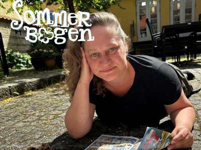 Børnebibliotekaren ligger og læser Anders And i bibliotekets gårdhave.