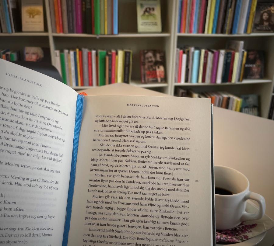 Bog og en kop kaffe foran en reol med bøger